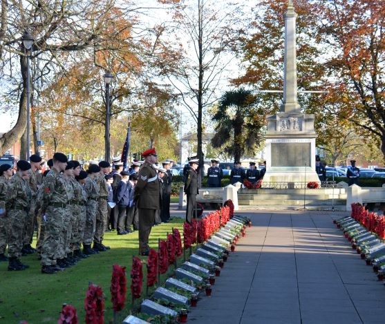 A coloured photograph of the Remembrance service in November 2018. There are members of the armed forces in uniform standing to attention next to Boston war memorial. The path is lined with red poppy wreaths.