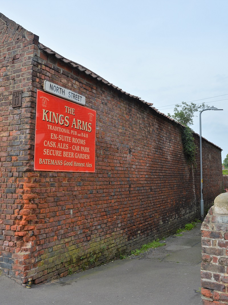 A photograph of North Street's road sign which is on a brick wall. Beneath the road sign is another, larger, red sign for The Kings Arms traditional pub and B and B.