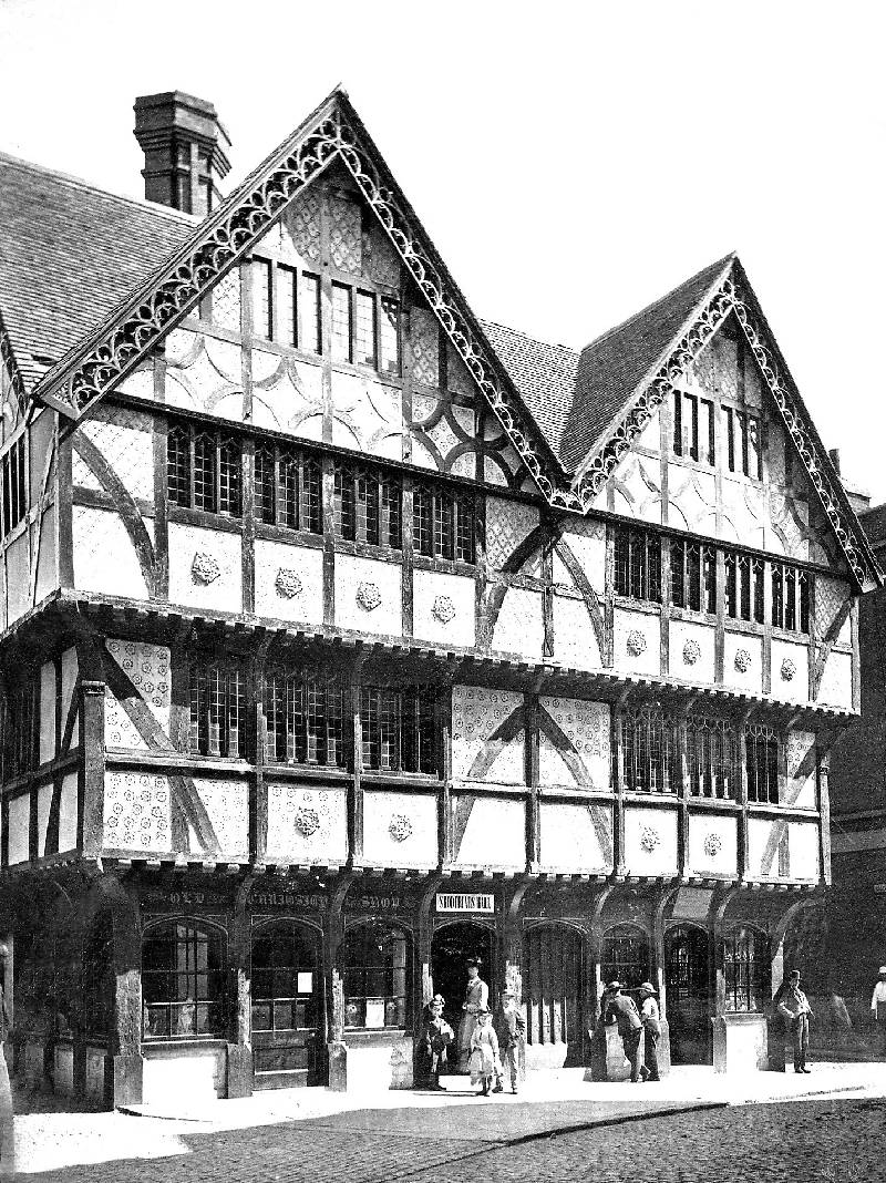 A black and white photograph of Shodfriars Hall in the year 1900. It has a wooden frame with ornate details in the eaves. Each of the upper two floors overhang the street below. The windows are large made up of individual leaded smaller panes. The bottom of the building is panelled in dark wood.